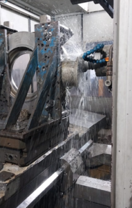 Usinagem mandrilhadora FEMES: peça metálica sendo usinada em mandrilhadora industrial com ferramenta de corte e refrigeração, ilustrando serviço de precisão da marca.