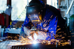 Imagem de um soldador usando máscara e equipamento de soldagem com faíscas em processo de união de metal, ilustrando tipos de soldagem da Femes Ferramentaria e Caldeiraria.